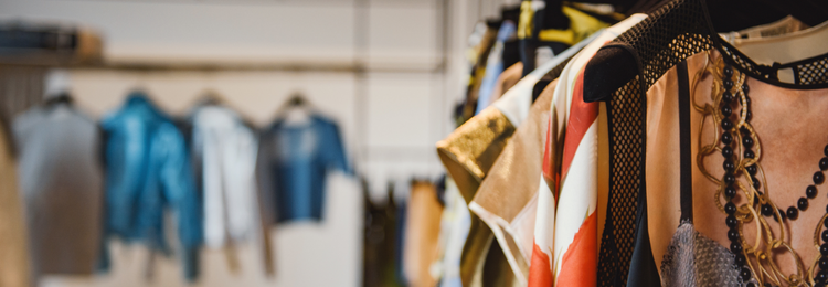 Assorted clothing items on hangers in a retail shop, with a focus on textures and colors, indicating fashion and shopping