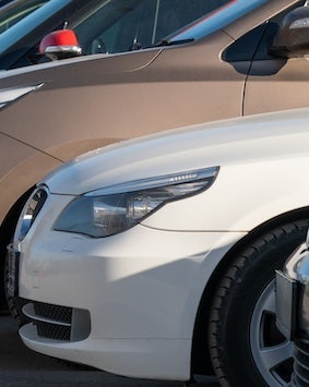 Close-up of a white car's front headlight and grille, with another vehicle in the background