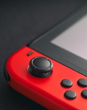 Close-up of a red game controller joystick and buttons on a dark background.