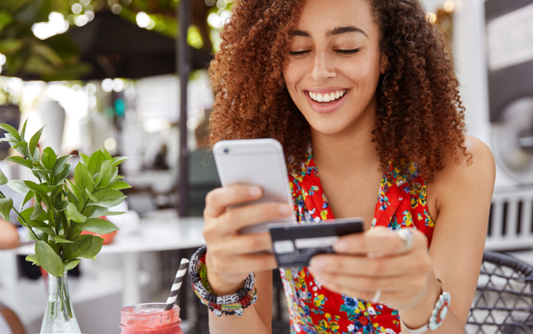 Image showing a smiling woman using a phone and holding a credit card, making a payment.