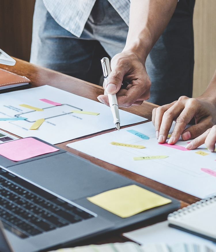 Image showing 2 people collaborating over a table with sticky notes, charts, and a laptop, focusing on planning