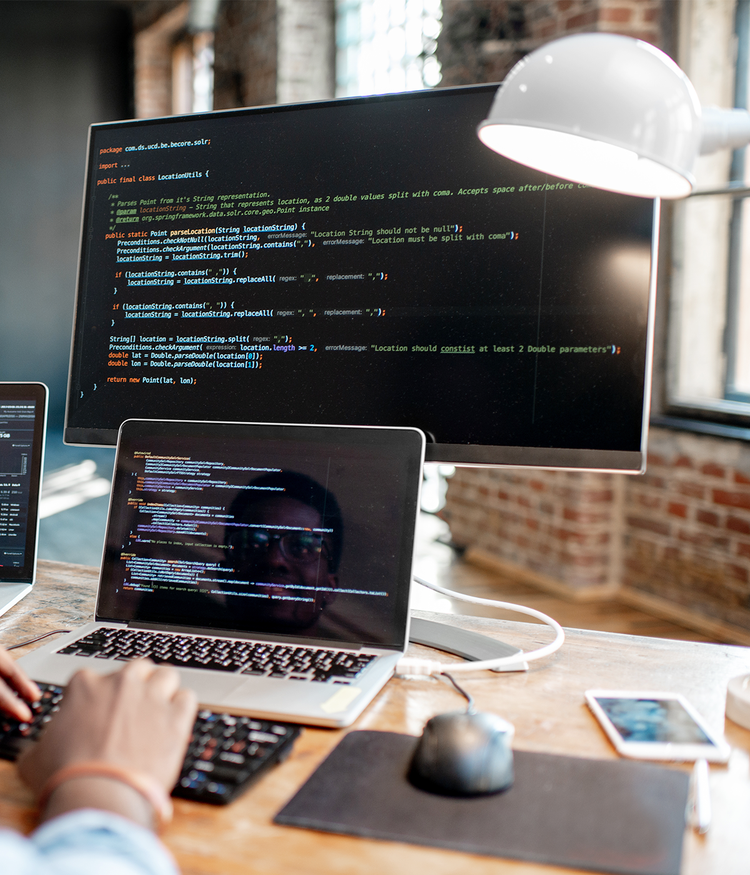 image showing a person typing on a laptop with code on the screen in a well-lit office environment