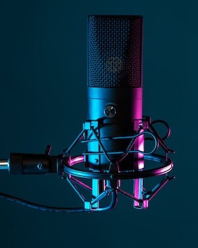 Studio microphone with a shock mount and pop filter against a dark blue background, highlighted by pink and blue lights