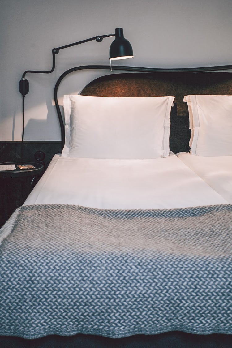 Hotel room bed with clean white linen and a wall-mounted lamp.