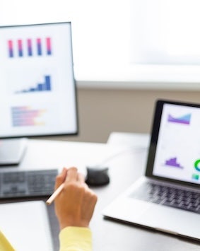 This is a blurred image showing an office setting with a person working on a laptop and a another display monitor