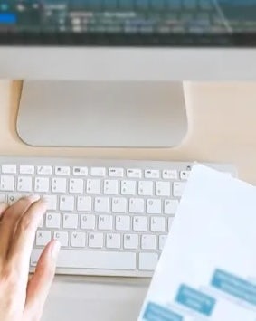 Person working on a computer with a white keyboard and blurred paper.