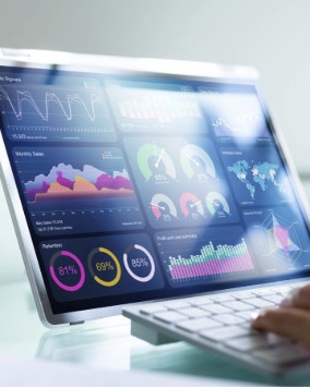 Image showing a computer screen with colorful data analytics and graphs, with a person's hand on the keyboard.